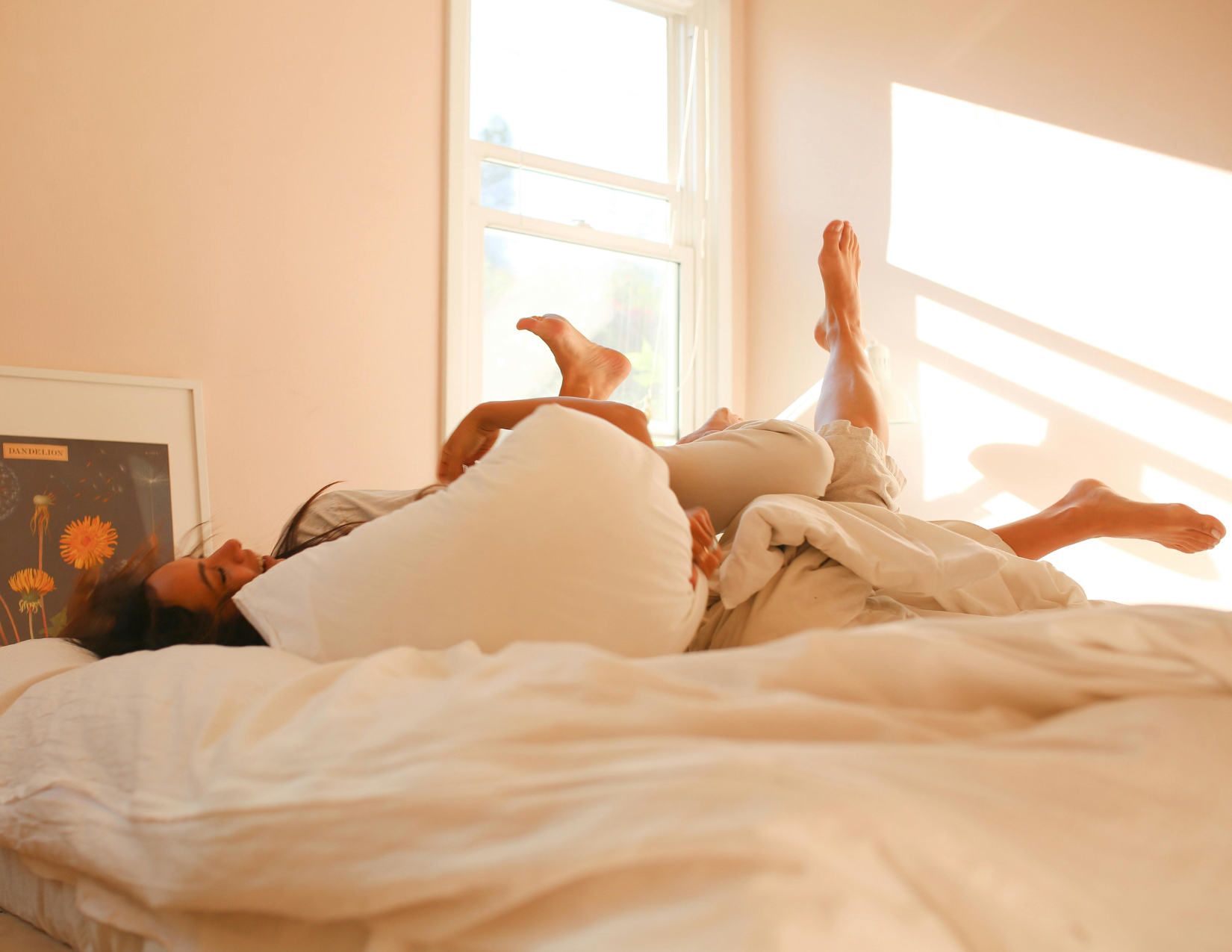 morning light with couple laughing and playing in bed in room with white room decor and natural light