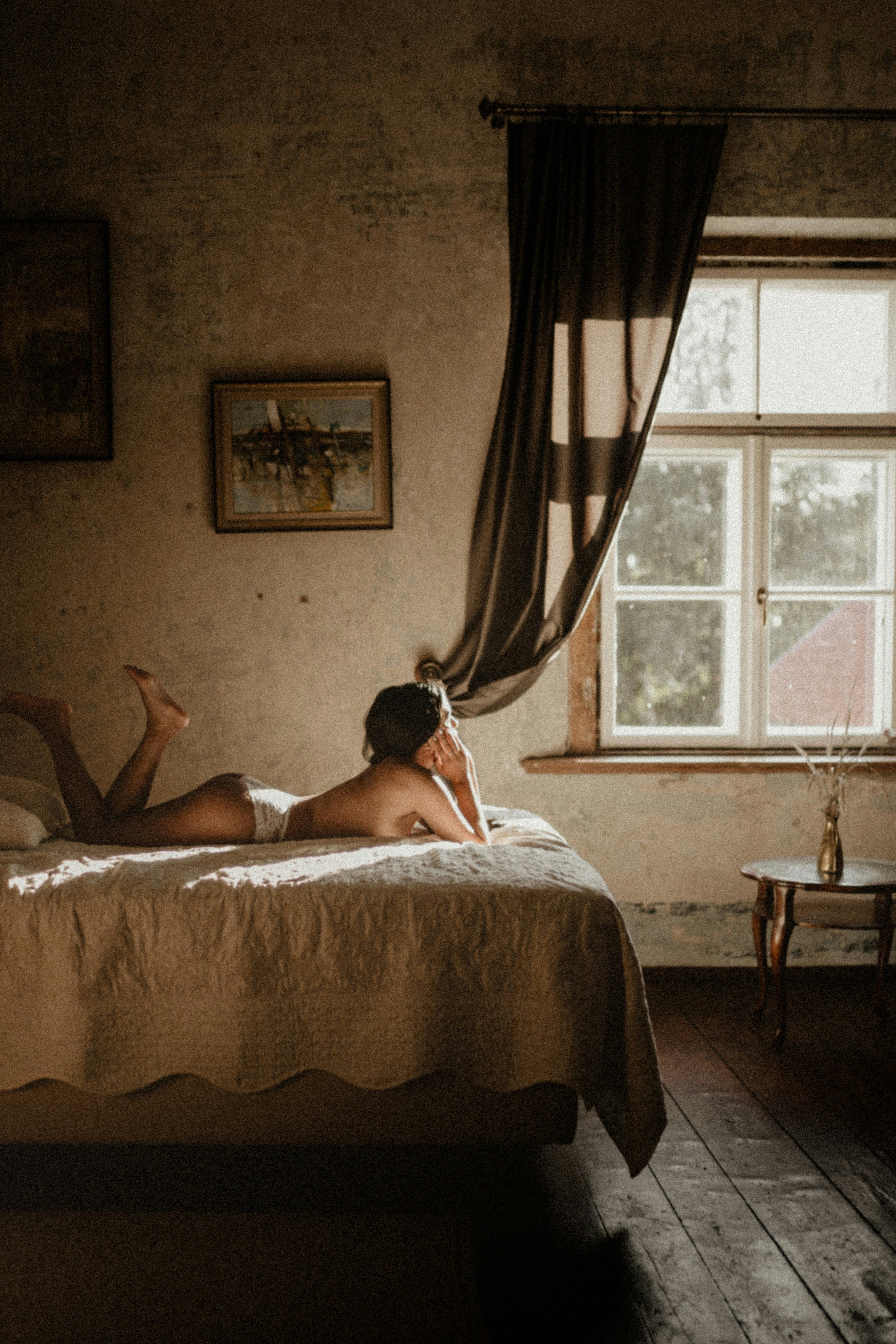 woman deep in thought and laying topless on bed in morning light through window
