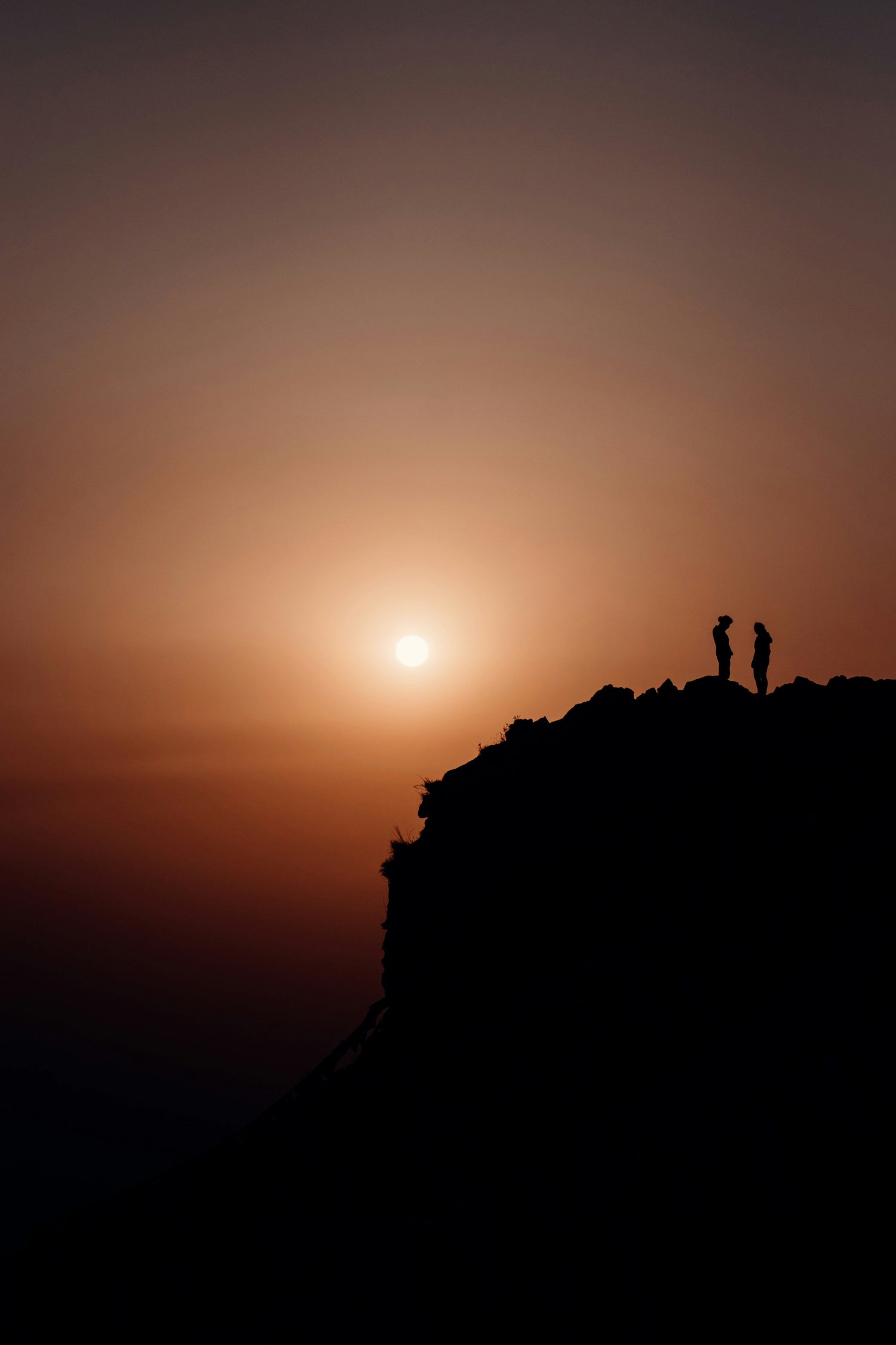 couple in distance reaching top of mountain at sunset