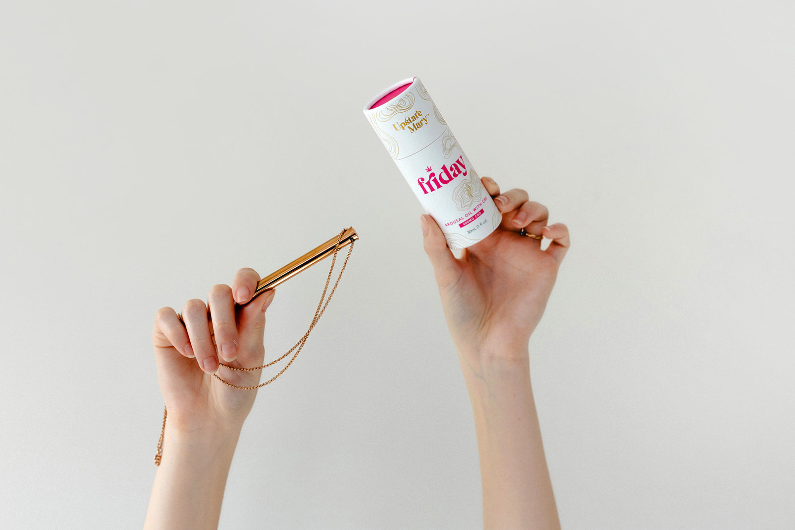 Person holding Friday arousal oil with a rose gold vibrator necklace against a plain background