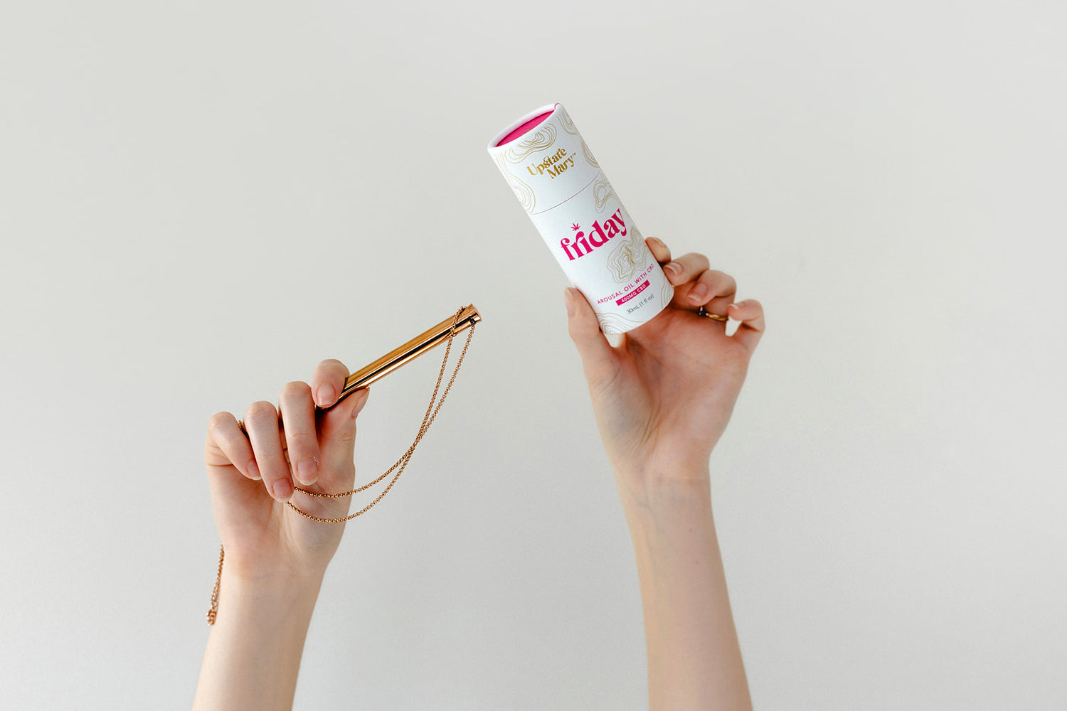 Person holding Friday arousal oil with a rose gold vibrator necklace against a plain background